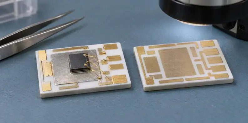 Two white ceramic circuits show gold-colored lands, a silver-colored attachment area and fine wires beside a dark die.